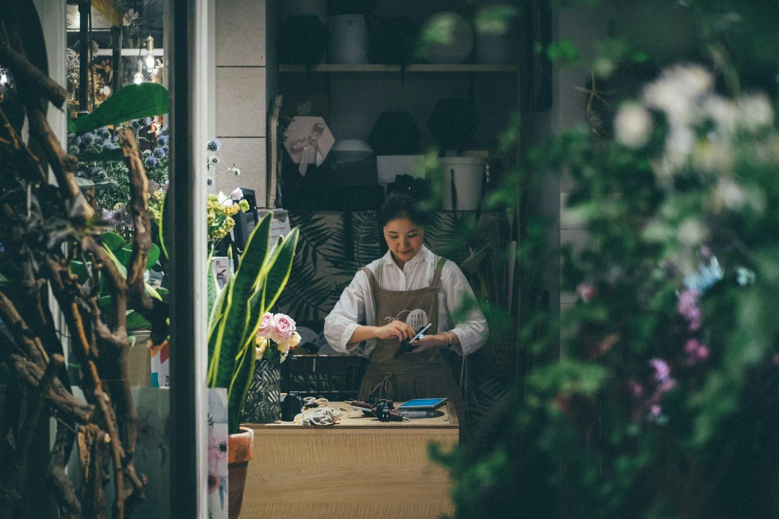 Fleuriste au travail derrière son comptoir, entourée de fleurs