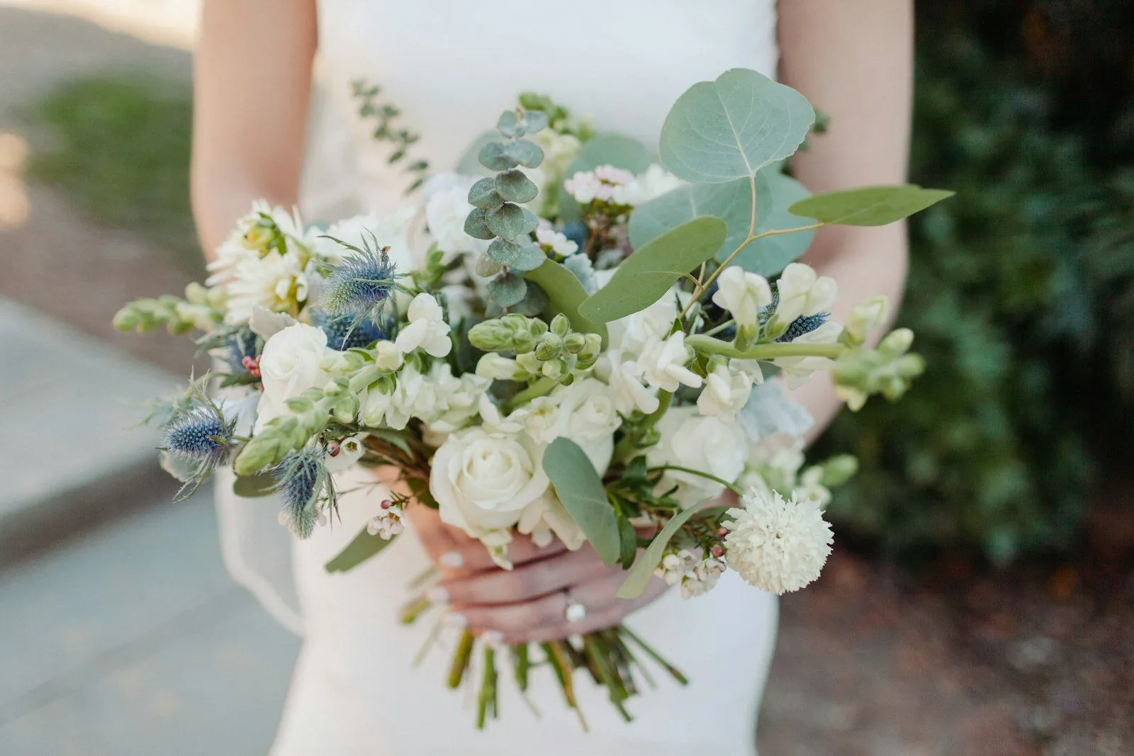 Mariée tenant un bouquet blanc et vert d’eucalyptus et de chardons