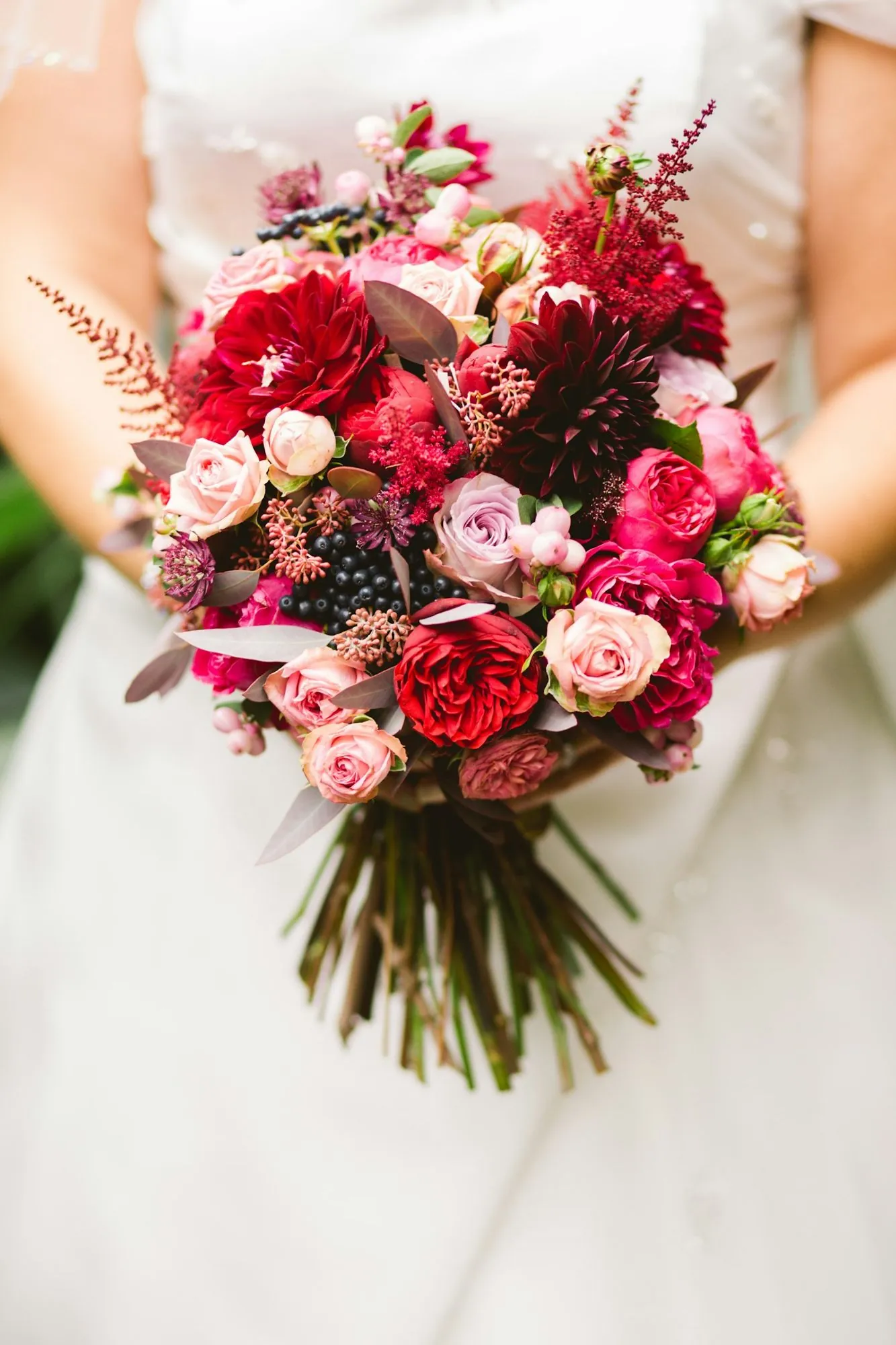 Mariée tenant un bouquet de roses rouges, pivoines et astilbes